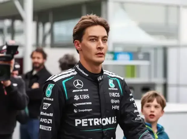 Titel-Bild zur News: George Russell im Mercedes-Overall: Halbportrait, neutraler Blick, geht durchs Paddock