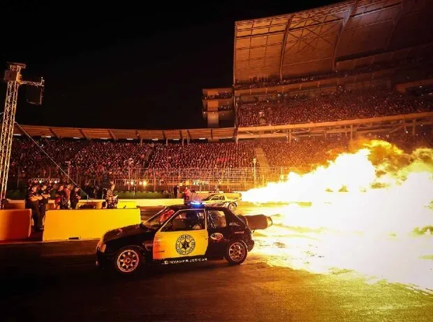A jet car in police design shoots a gigantic fire roll from the aircraft turbine during the nighttime NitrOlympX Nightshow at the Hockenheim Motodrom in front of fully occupied spectator stands.