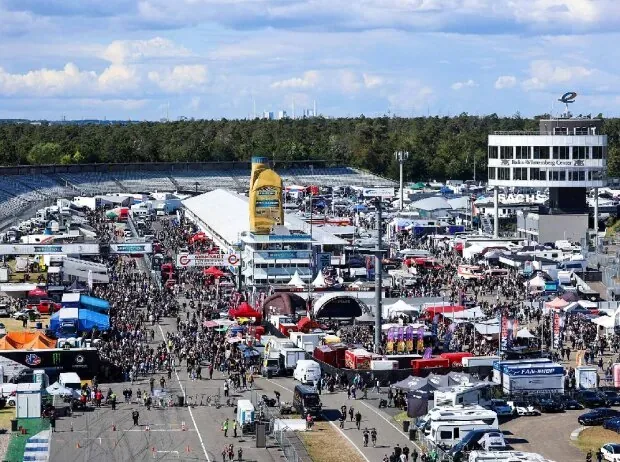 Aerial view of the huge, freely accessible paddock of the NitrOlympX at the Hockenheimring, with countless team tents, trucks, and motorsport fans in front of the stands.